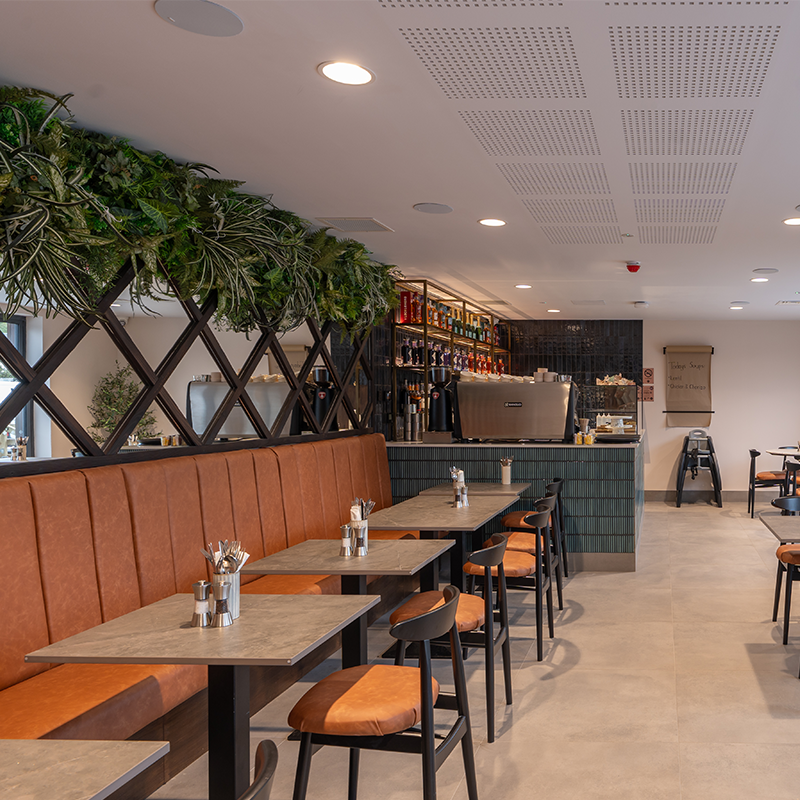 Modern restaurant interior with orange booths, tables, and a bar area.