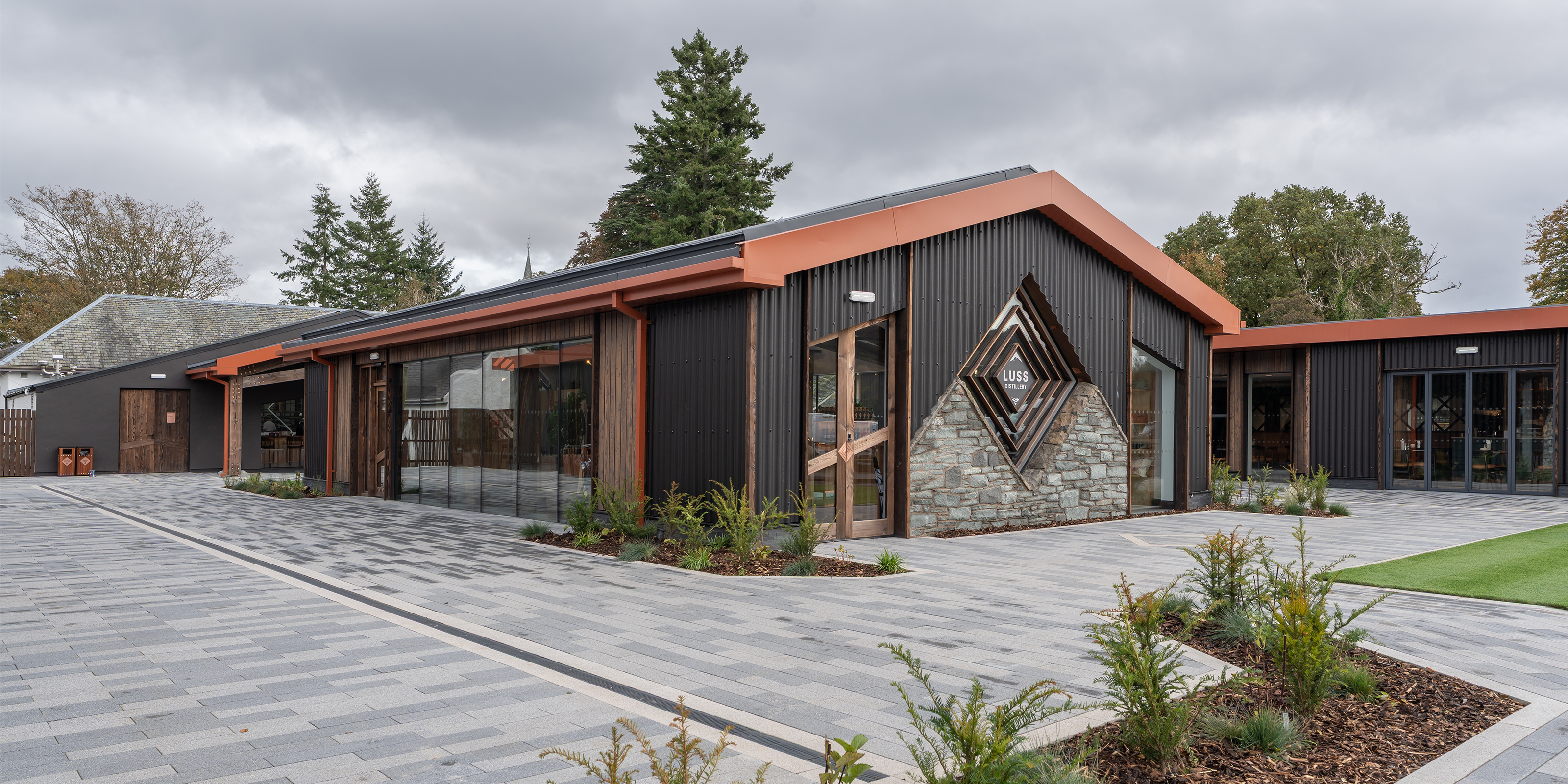 Modern building with a geometric design on the roof, surrounded by trees and a paved area.