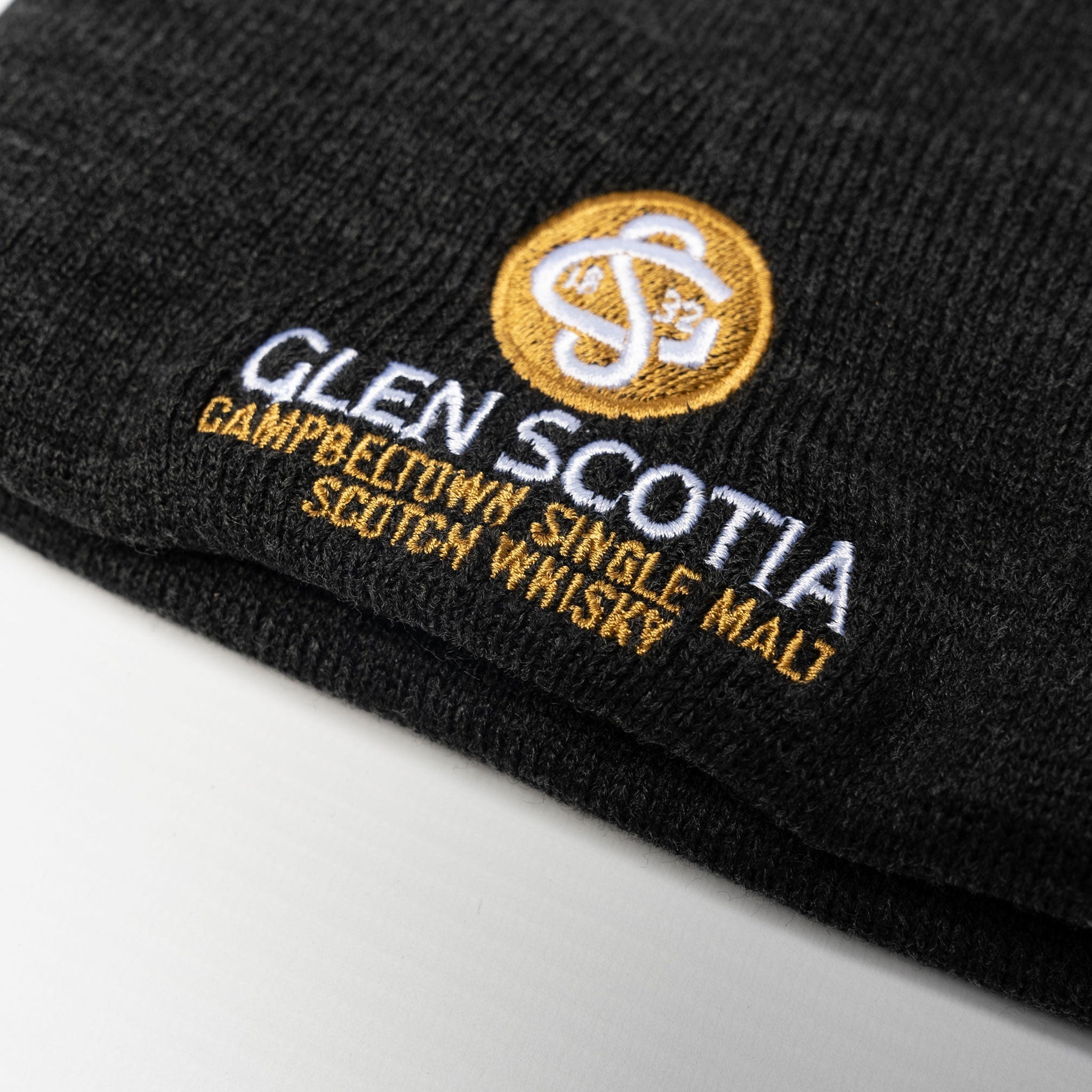 Close-up of a Glen Scotia Grey Beanie Hat featuring the embroidered logo and text for "Glen Scotia Campbeltown Single Malt Scotch Whisky" in white and gold thread. The logo includes interlocking letters "GS" within a circular design, making it an ideal gift for whisky enthusiasts.