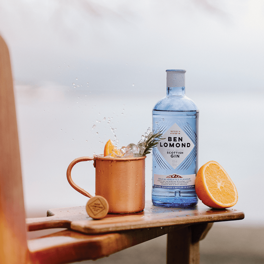Ben Lomond Scottish Gin bottle with a copper mug and orange on a wooden surface.